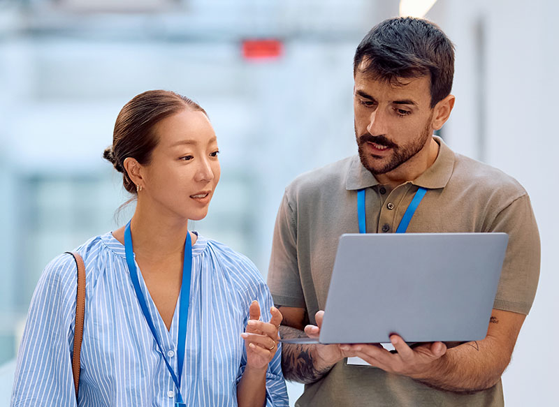 Bild – Kollegen, die im Flur eines Bürogebäudes etwas auf dem Laptop besprechen