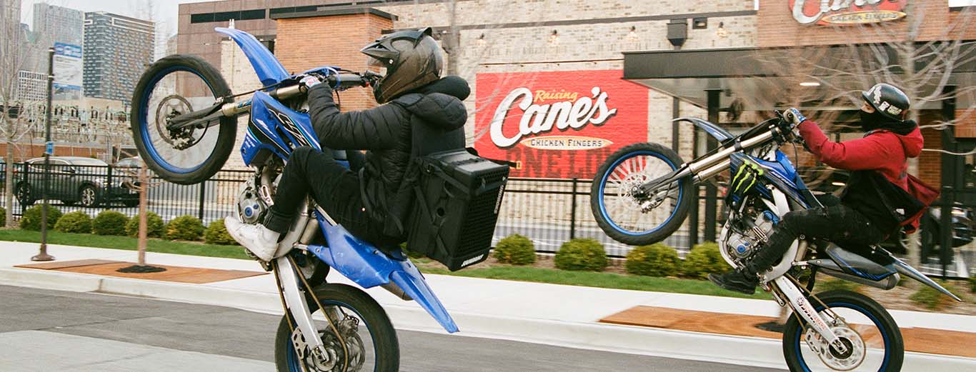Image-Motorcycles racing and doing wheelies on an urban stree with a Soundboks Bluetooth speaker strapped on the back.
