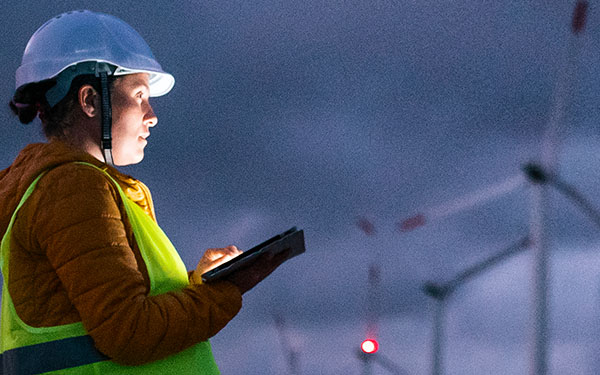Image-Engineer using a tablet at nightfall in a windfarm, dramatic lighting.