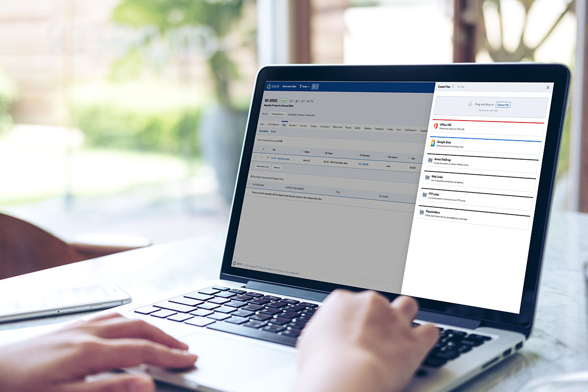 Why Integrating Cloud PLM With Microsoft 365 and Google Docs Is a Game Changer Image-Person using laptop with Arena Cloud Documents Connection software on vintage wooden table in cafe
