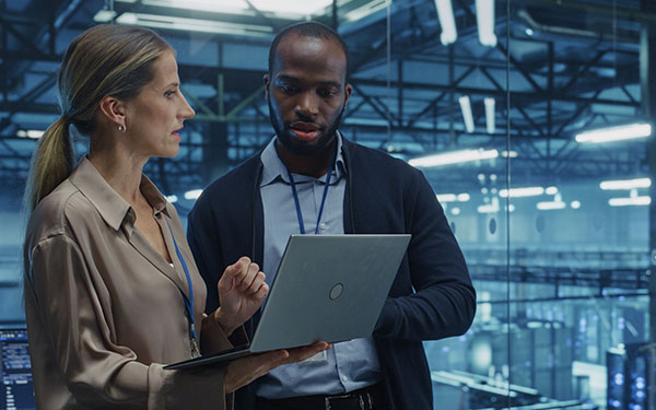 Image-Cloud Architect and Female Database Engineer Review Data Storage Protocols on a Shared Laptop in a Data Center