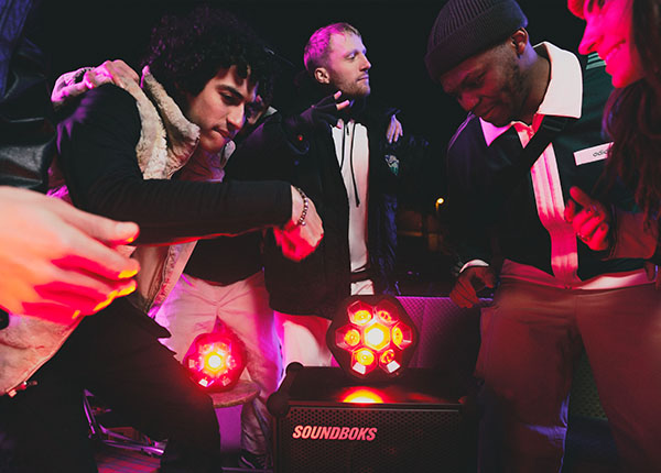 Image-Party/disco atmosphere with people dancing and Soundboks speakers and lighting systems in the center.