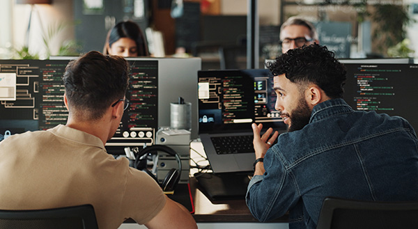 Image-Two developers discussing whats on screen, in a office environment with other developers